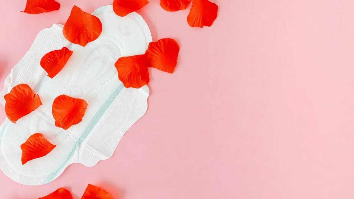 sanitary pad on a pink background with red flower petals symbolizing menstruation