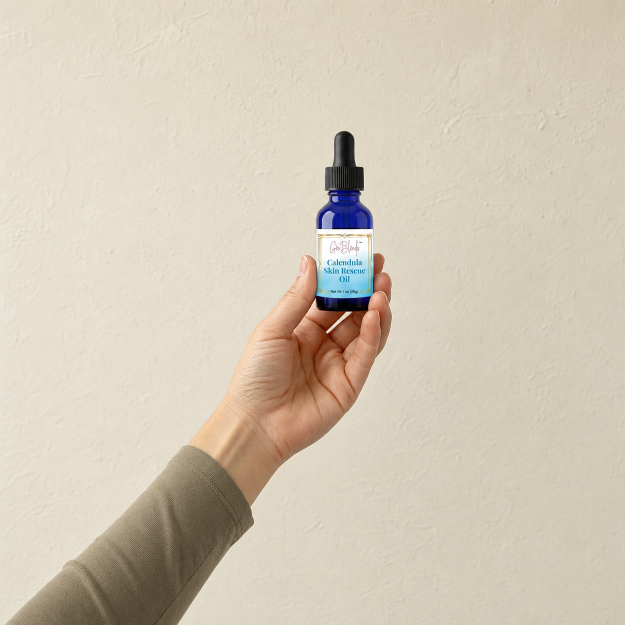 Hand holding a blue bottle of Calendula Skin Rescue Herbal Oil against a beige background